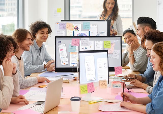 Diverse development team collaborating in a bright Minneapolis office with post-it notes and monitors showing brain-training app designs
